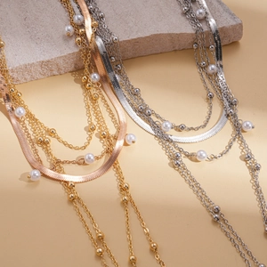 Detail view of multi-layer metallic chain necklaces with pearls and a teardrop pendant