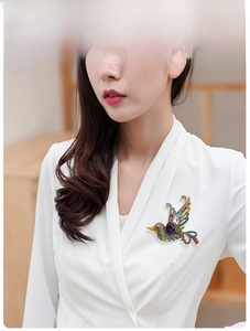 Detail of a colorful crystal bird brooch with purple droplet stone on a white shirt