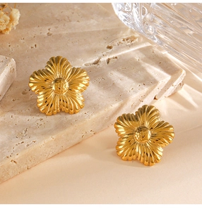 Detailed close-up of golden sunflower earrings with textured petals on a stone tray