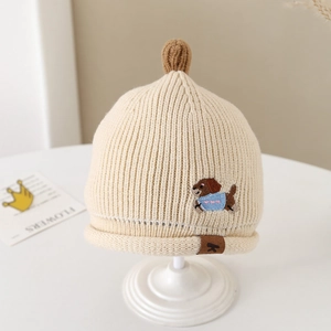 Détail d'un bonnet en tricot pour bébé avec broderie chiot et pompon doux