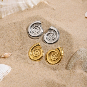 Orecchini a spirale a forma di conchiglia in oro e argento su sfondo di sabbia marina