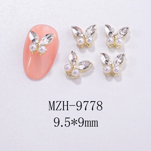 Macro shot of 3D gold butterfly nail art charms with pearls and rhinestones on white base