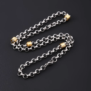 Macro detail of silver and gold stainless steel Cuban chain necklace on black backdrop