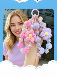 Dettaglio di ciondoli per cellulare con fiori all'uncinetto e pompon di peluche.