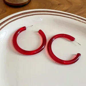 Fashionable red resin C-shaped hoop earrings with silver needle on white ceramic plate