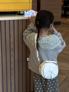 Girl wearing a white round crossbody bag with a large bow and adjustable strap in a cafe