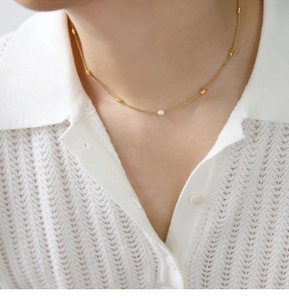 Detail of 18K gold plated necklace with pearls on a model wearing white knitwear