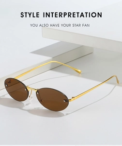 Detail of rimless oval sunglasses with gold metal frame and brown lenses on white blocks