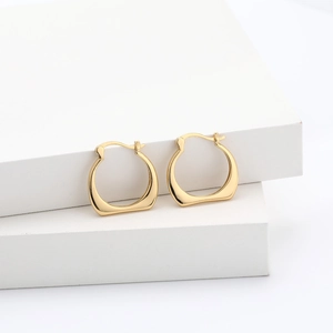 Vue détaillée de boucles d'oreilles créoles dorées géométriques sur supports blancs