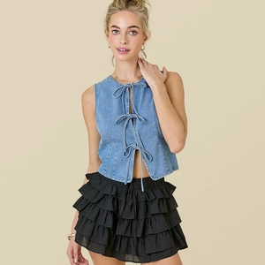 Detailed view of trendy blue denim lace-up vest paired with a layered black ruffle skirt