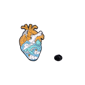 Detail of anatomical heart enamel pin featuring a blue ocean, whale, and orange sunset