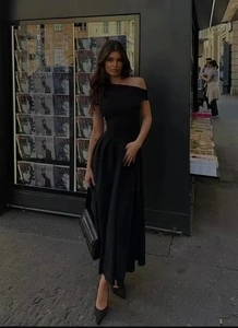 Detalle de vestido largo negro con hombros descubiertos, talle ajustado y bajo acampanado