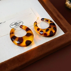 Macro detail of tortoiseshell C-shaped resin earrings inside a vintage jewelry box