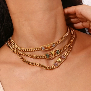Détail de chaînes cubaines en or 18K superposées avec pendentifs cœur et zircons colorés