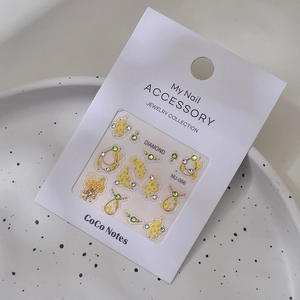 Detail of 3D floral nail art charms with yellow flowers and green rhinestones in package