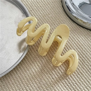 Close-up of a beige wavy hair claw clip placed on a woven mat with natural lighting