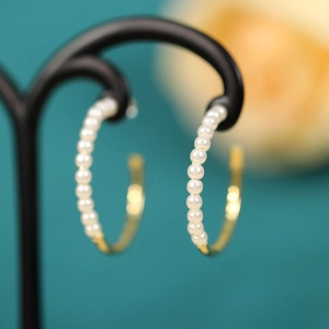 Close-up of pearl hoop earrings with gold finish on a black professional jewelry stand