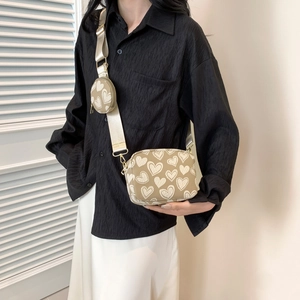 Detail of a chic beige heart-pattern crossbody bag with a wide strap and mini round pouch