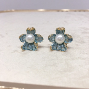 Macro shot of blue flower earrings with a white pearl center and golden edges