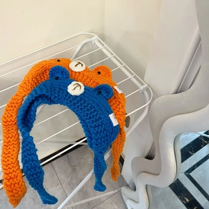 Knitted animal style baby winter hats in orange and blue on a white metal rack