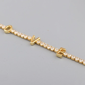 Macro detail of gold-plated tennis necklace featuring LOVE zircon-set letter charms