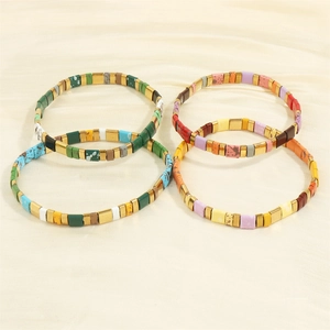 Macro shot of colorful Tila tile bracelets with enamel beads on white silk background