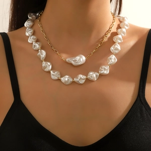 Macro detail of layered baroque pearl necklace with gold chain on model's neck