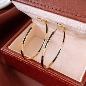 Detailed close-up of 14k gold hoop earrings with black enamel and zircon inlay on a leather box