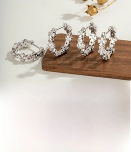 Détail de créoles argentées avec incrustations de zircon rose et blanc sur bois