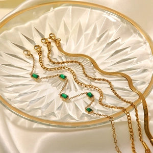 Detail von vergoldeten Armbändern mit grünem Zirkon auf Kristall und weißer Seide
