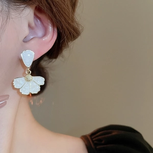 Close-up detail of white enamel petal flower earrings with gold center worn by a model
