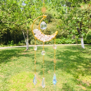 Detail of moon-shaped gold suncatcher with pink crystals and sun charms on garden background