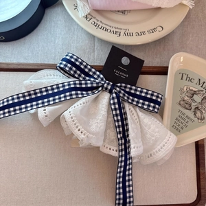Detailed shot of bow hair clip with blue plaid pattern and white lace embroidery trim