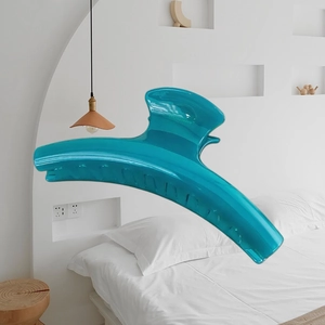 Large 15cm cyan blue shark hair claw clip in a minimalist bedroom setting