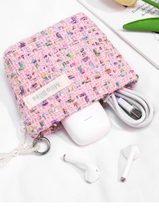 Detailed macro view of pink tweed coin purse holding white earphones and charging cable