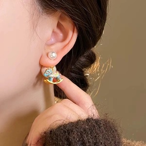 Detailed view of rocking horse pearl earrings worn by model with gold enamel finish