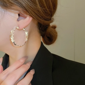 Close-up of a model wearing large silver wavy hoop earrings with a polished metallic texture