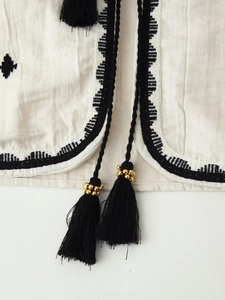 Close-up of white cotton-linen fabric featuring black embroidery and beaded tassels