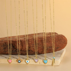 Gold evil eye pendant necklaces with heart and feather shapes on marble background