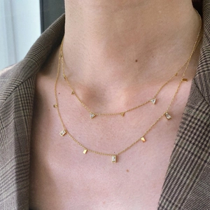 Close-up of layered gold titanium steel necklaces with triangular and rectangular zircon charms