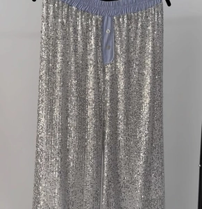Detail of silver sequined high-waisted wide-leg pants with striped placket and buttons