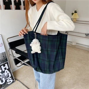 Plaid wool tote bag with plush sheep charm detail shown in a minimalist home setting