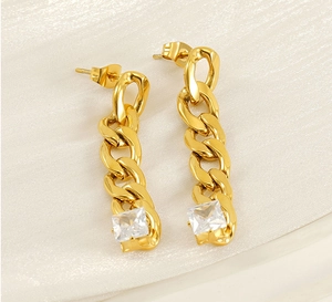 Detailed close-up of gold chain earrings featuring square cubic zirconia on white silk