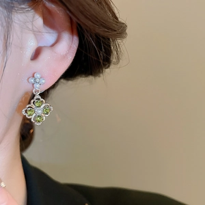 Close-up of floral pearl earrings with green gemstone clover charms worn by a model