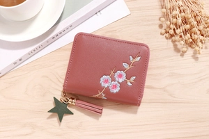 Detail of rose pink leather wallet with floral embroidery, tassel, and star charm
