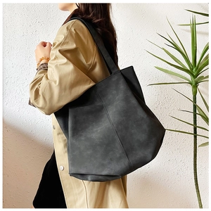 Detail view of large dark grey faux leather tote bag worn with a stylish trench coat