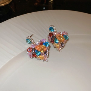 Macro detail of heart-shaped colorful gemstone cluster earrings on a white ceramic tray