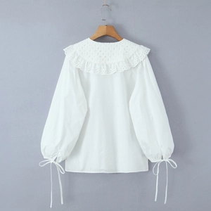 Detalle de blusa blanca con cuello Peter Pan de encaje y lazos en las mangas de linterna