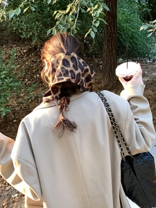 Detail of a leopard print satin hair scarf styled on a low ponytail with a beige coat