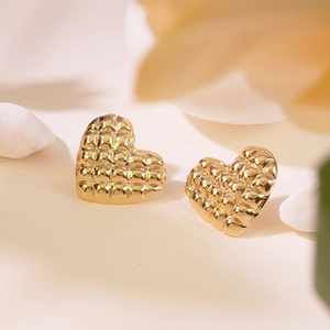 Detail of gold heart earrings with quilted texture on an elegant warm background